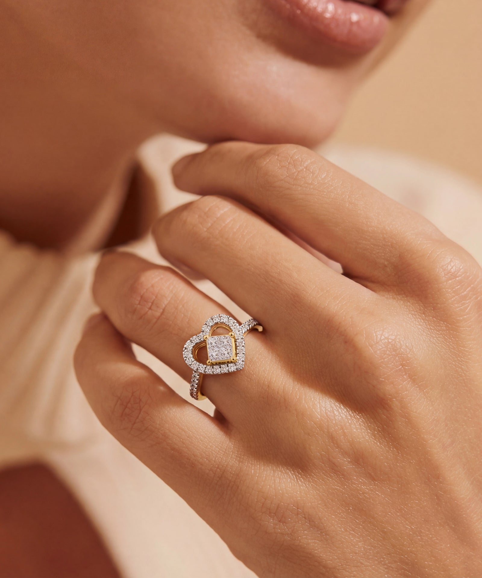 Close-up of a hand wearing a diamond ring with a heart-shaped center on a soft beige background.