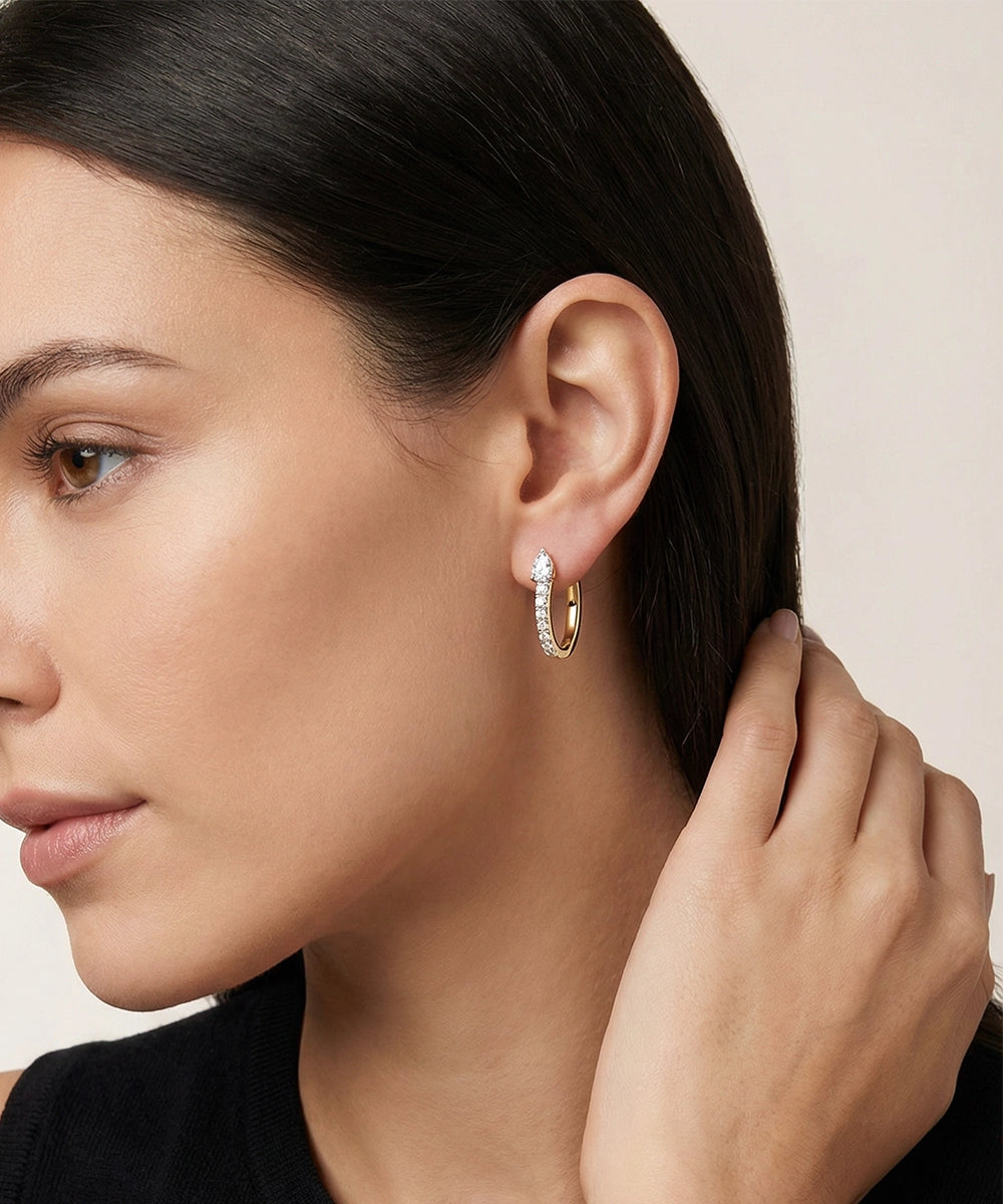 Close-up of a woman wearing gold hoop earrings with a neutral background
