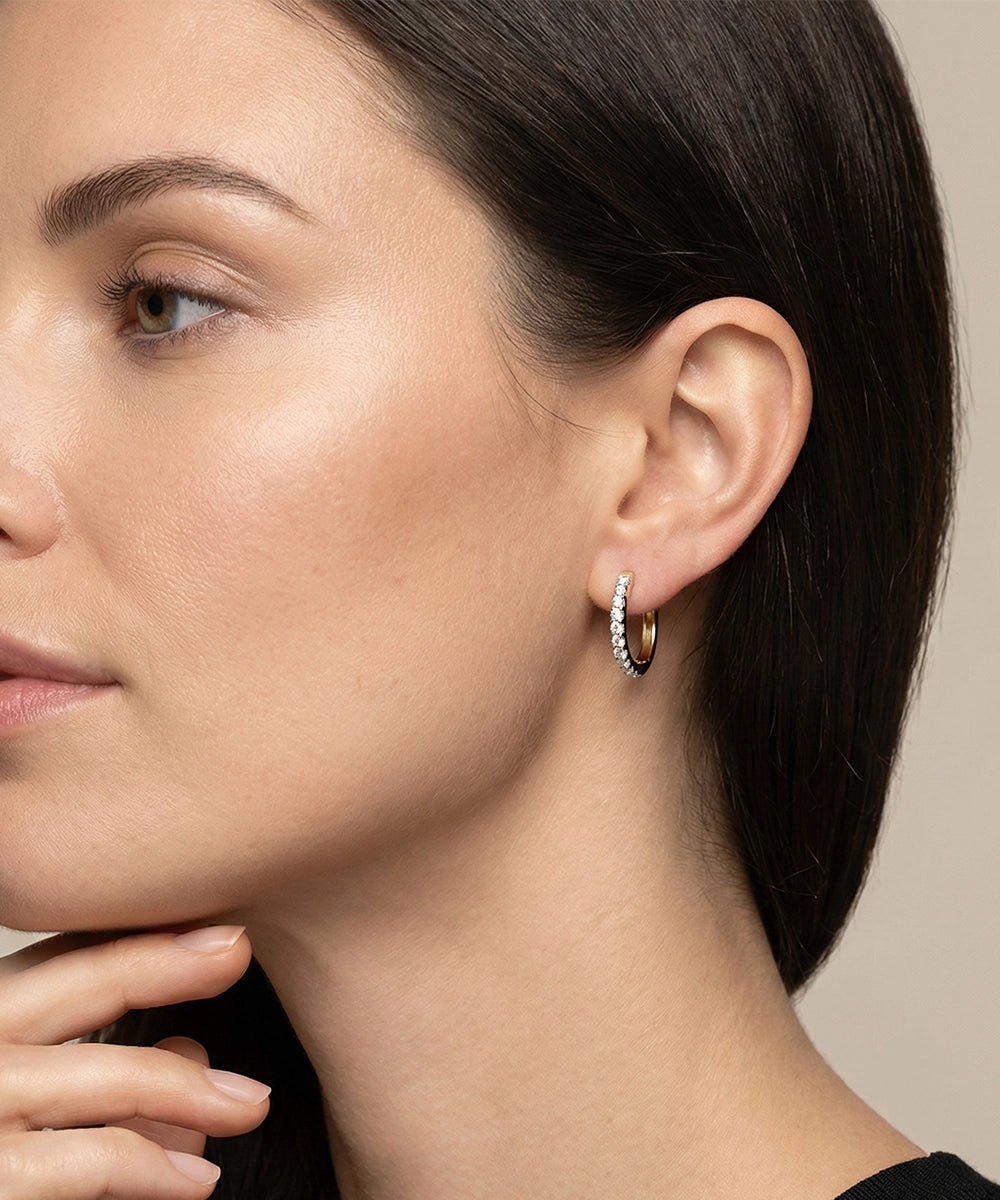 Close-up of a woman wearing gold hoop earrings with a neutral background