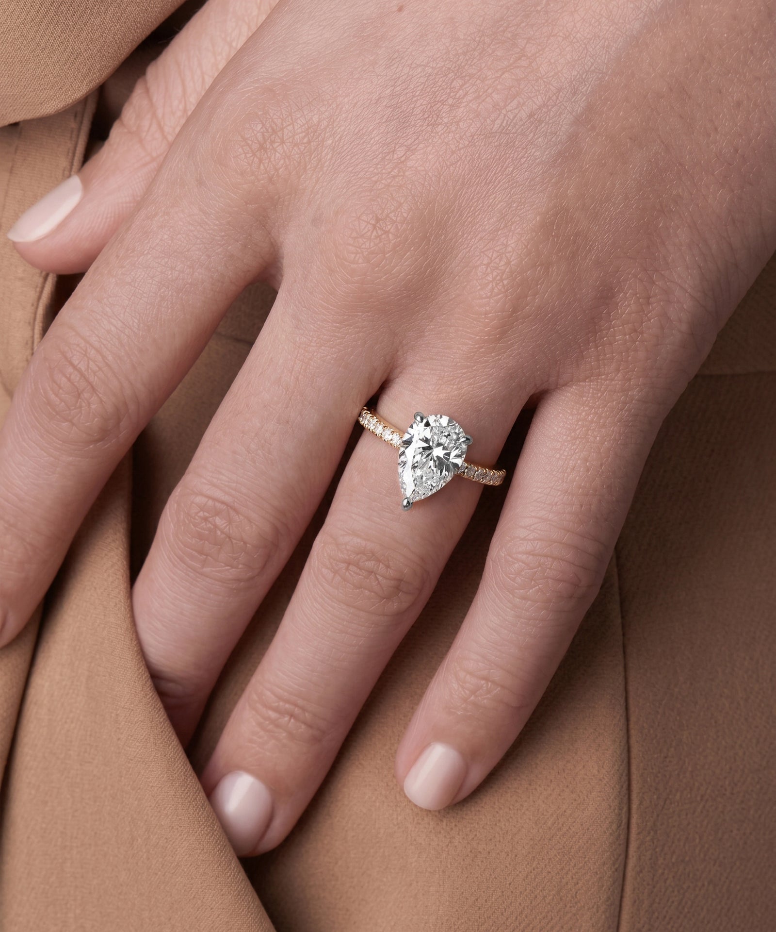 Close-up of a hand wearing a diamond ring on a brown fabric background
