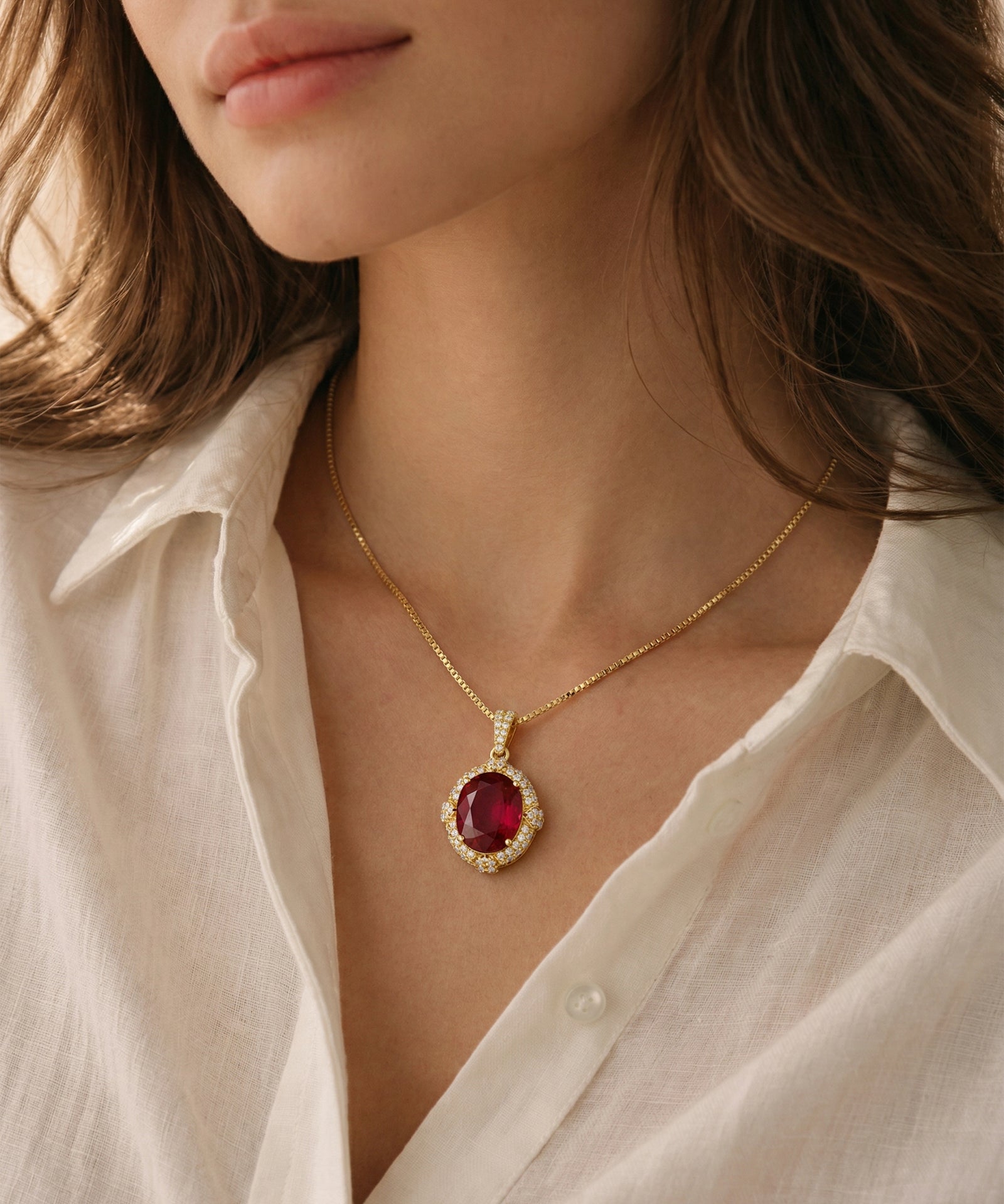 Oval ruby halo pendant necklace on a yellow gold chain shown on a model.
