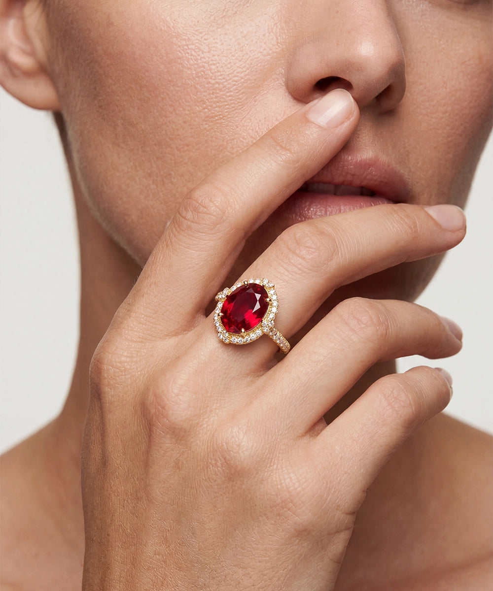 Close-up of a hand wearing a ring with a red gemstone, touching the lips.