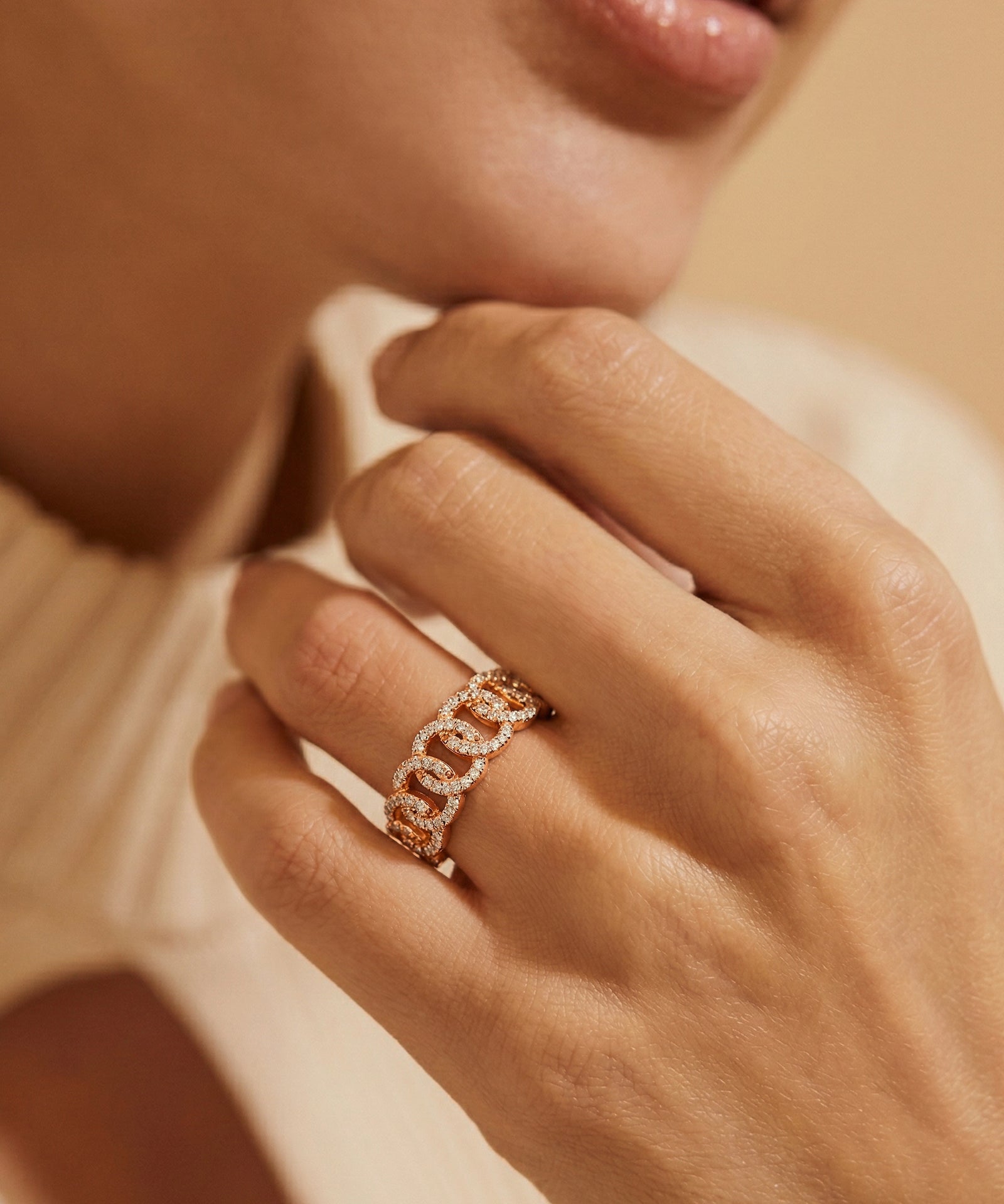 Close-up of a hand wearing a rose gold chain-link ring with a soft focus background