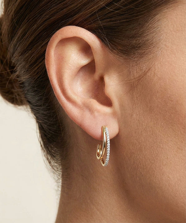 Close-up of an ear wearing a gold hoop earring with a clear gemstone.