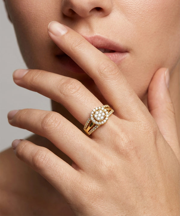 Close-up of a hand wearing a gold ring with a diamond cluster, touching the face.