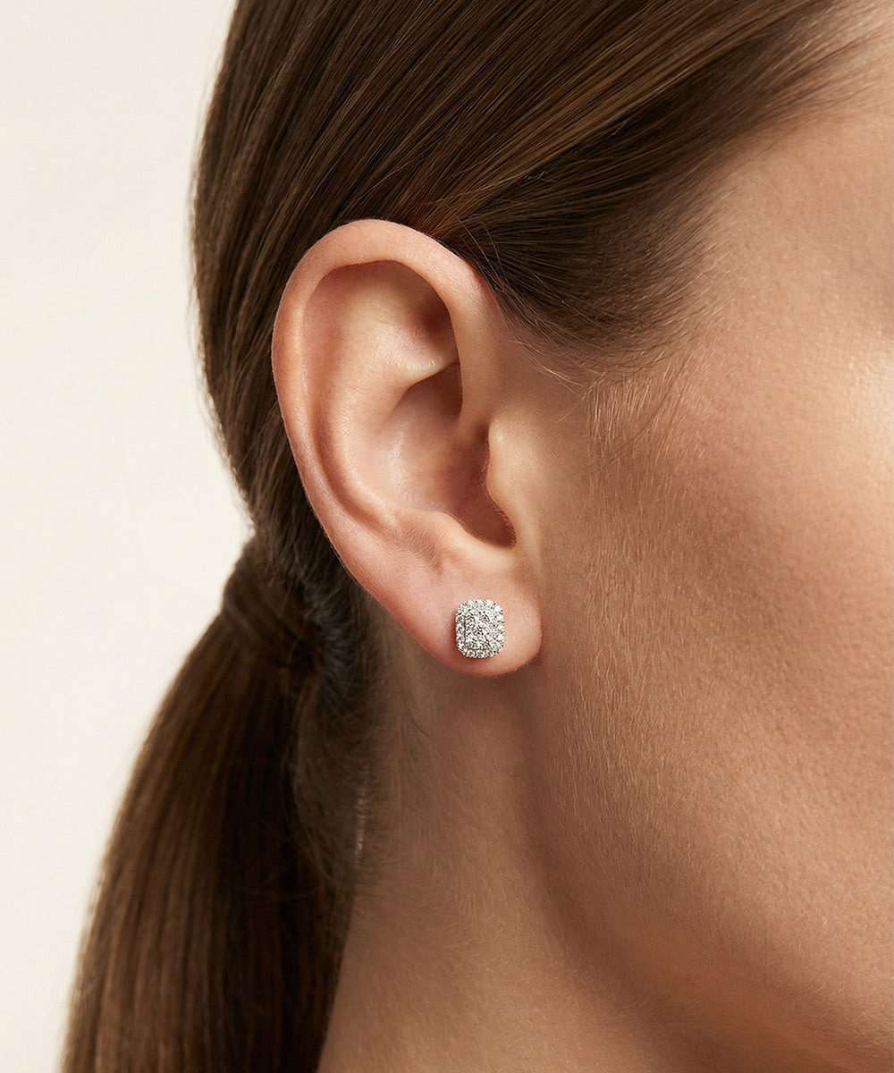 Close-up of an ear wearing diamond stud earrings with a neutral background
