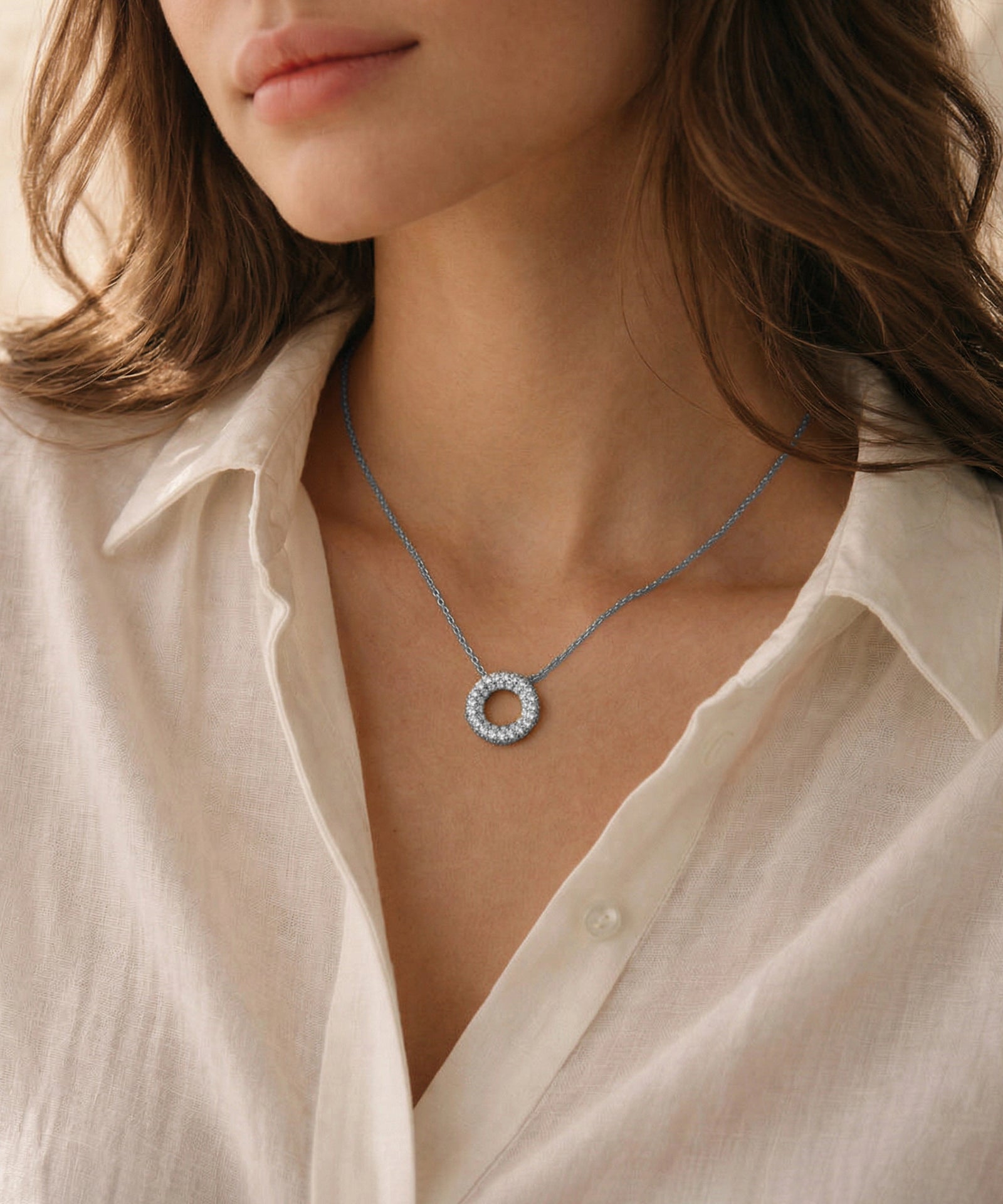 Necklace with a circular pendant worn by a person in a white shirt.