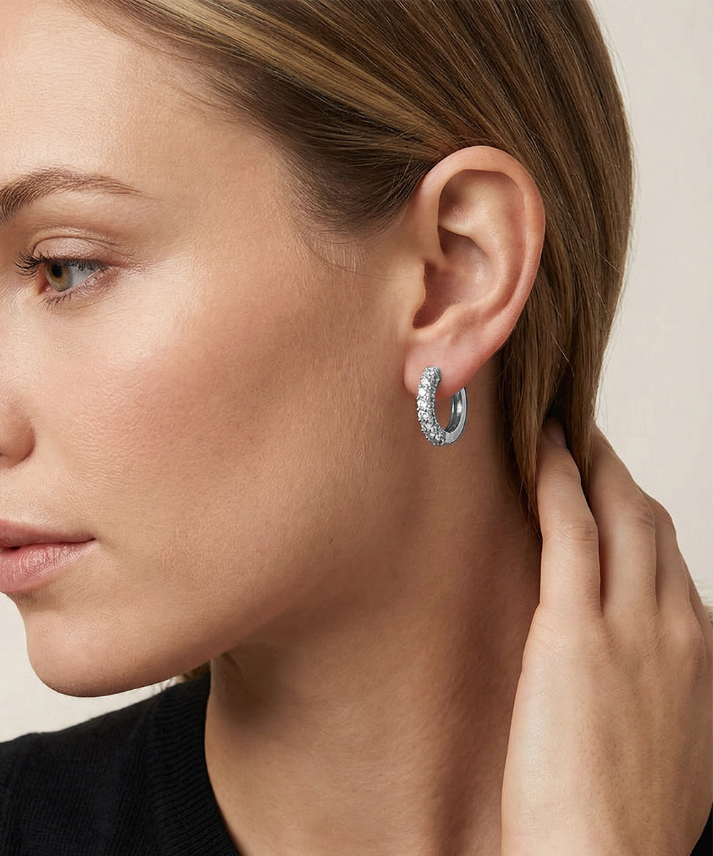 Close-up of a woman wearing silver hoop earrings against a neutral background