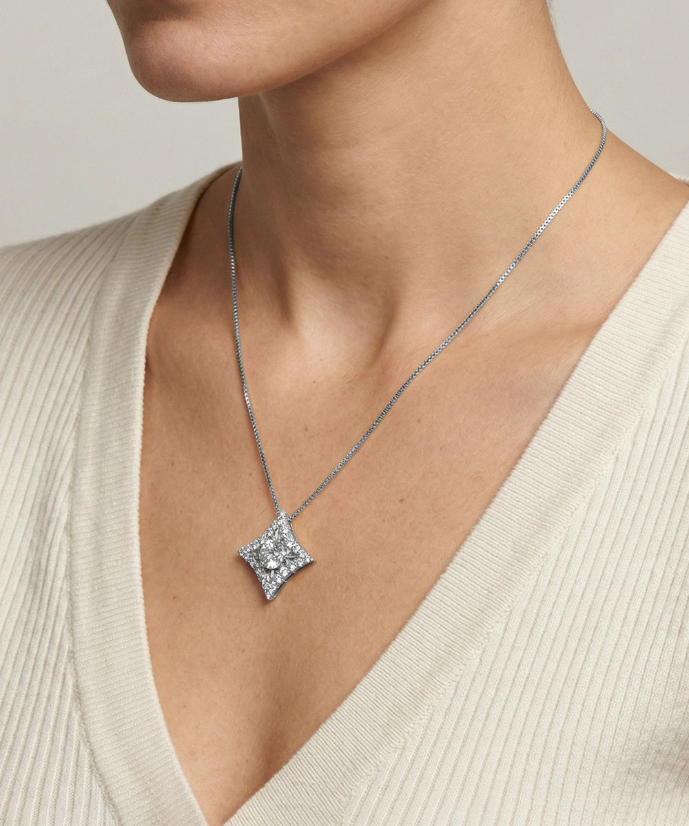 Silver necklace with a square pendant worn by a person in a beige sweater.