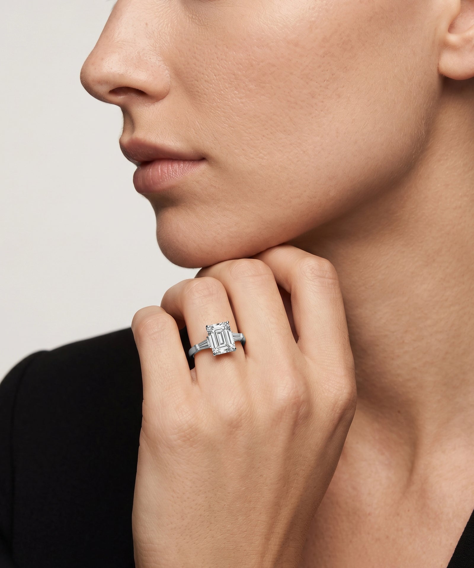 Close-up of a woman's hand wearing a diamond ring on a neutral background