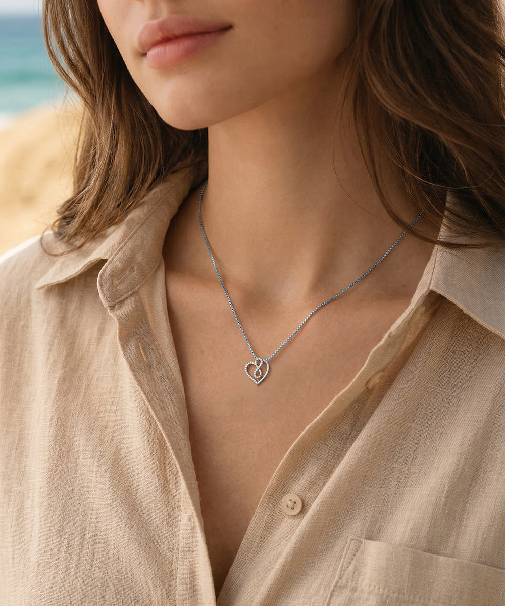 Close-up of a person wearing a gold necklace with a heart pendant, set against a blurred natural background.