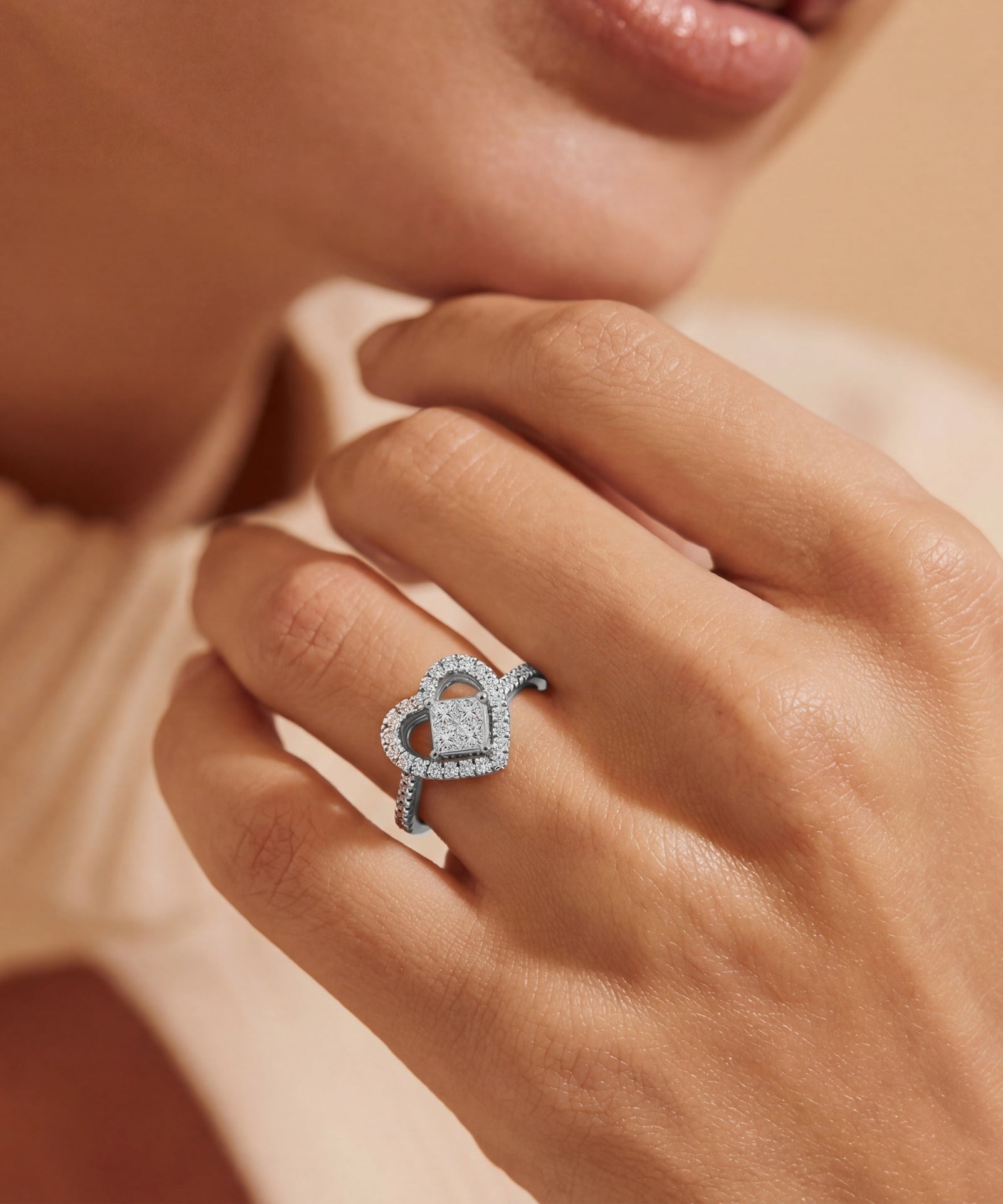 Close-up of a hand wearing a diamond ring with a heart design on a neutral background