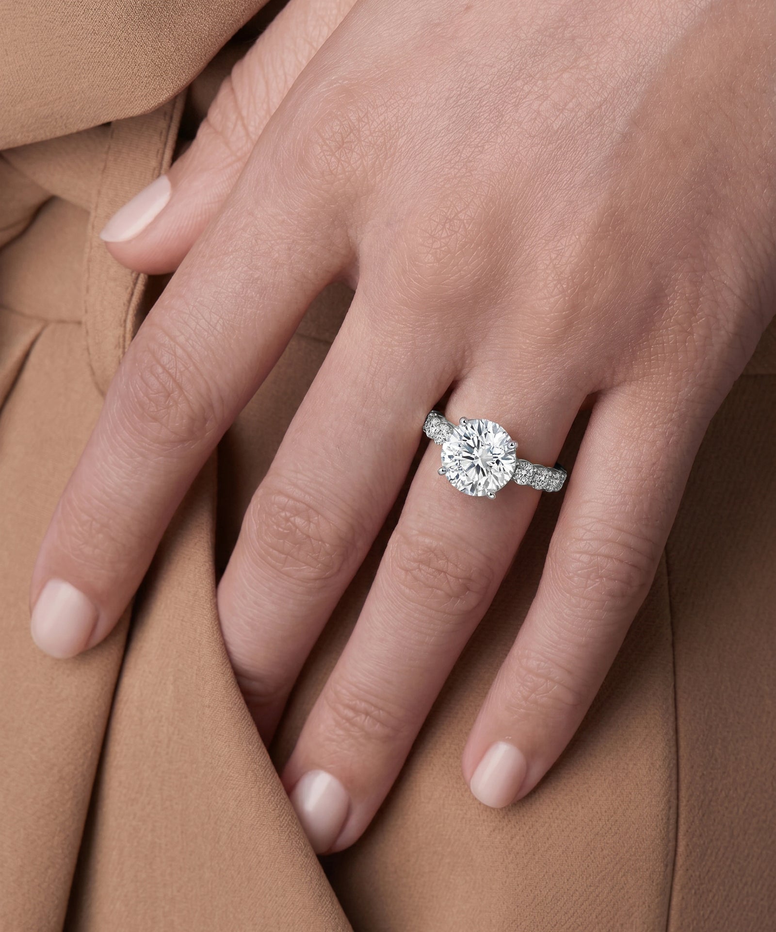 Close-up of a hand wearing a diamond ring on a brown fabric background