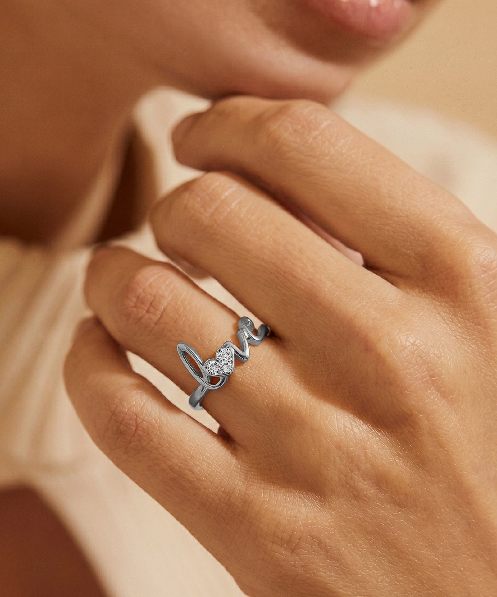 Silver 'love' ring on a person's finger with a blurred background