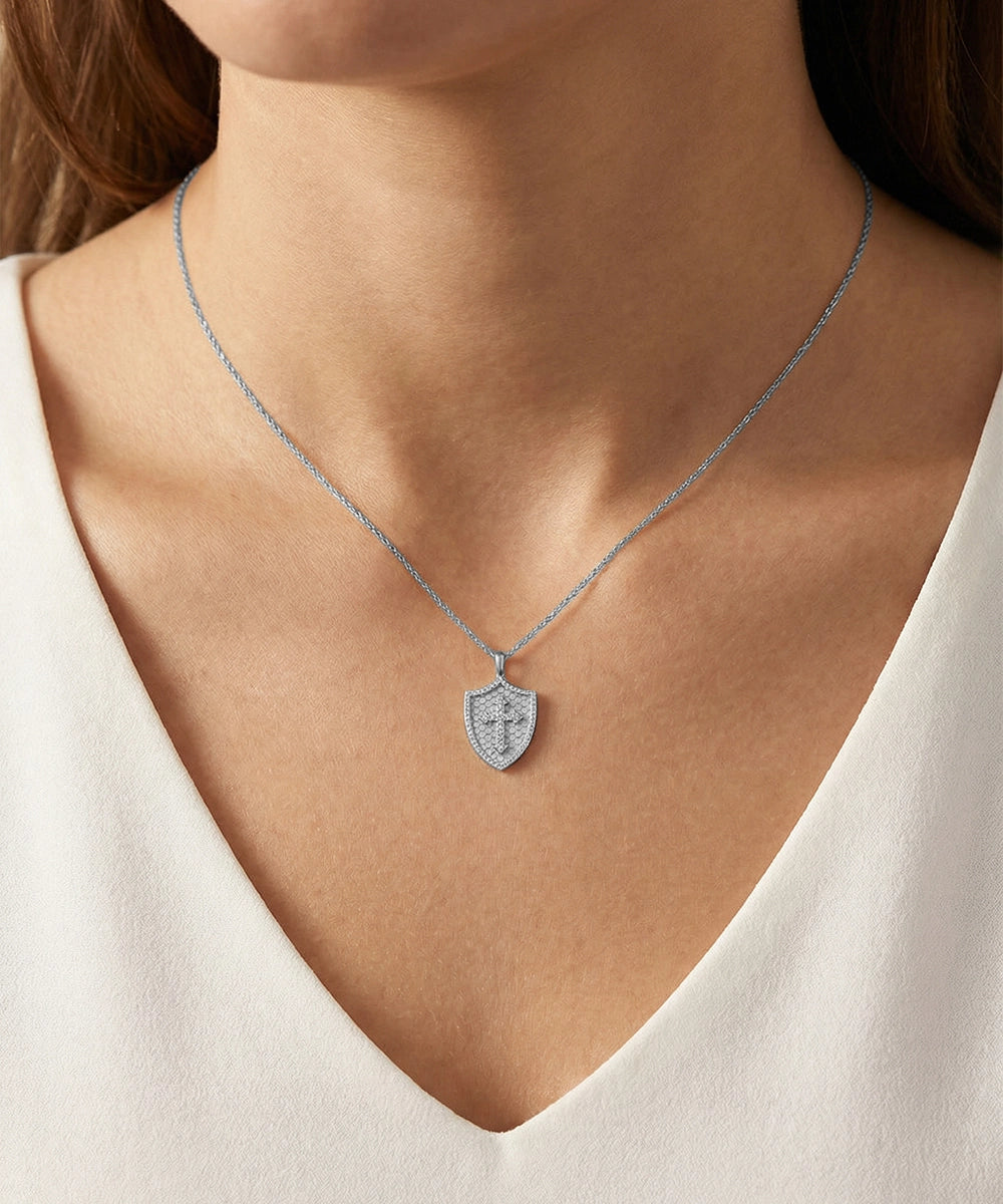 Silver necklace with a shield pendant worn by a person in a white top.