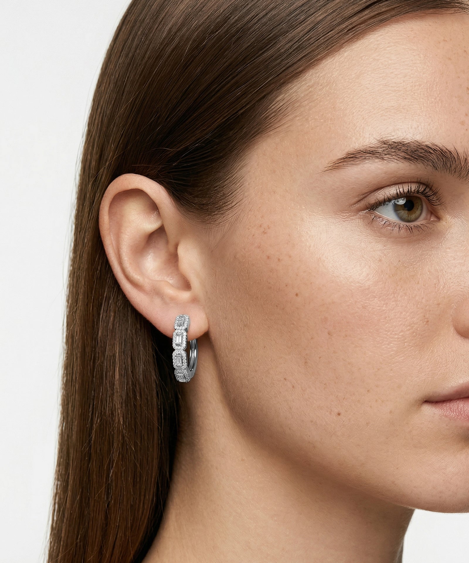 Close-up of a woman wearing silver hoop earrings with a plain background
