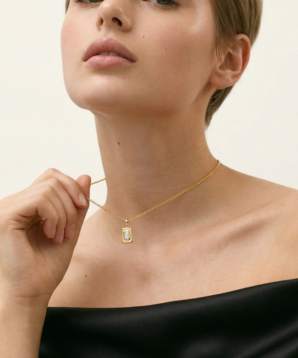 Woman wearing a gold necklace with a rectangular pendant against a neutral background