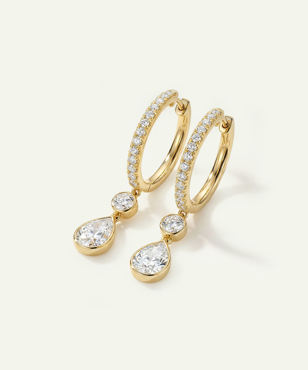 Gold hoop earrings with teardrop-shaped diamond pendants on a light background