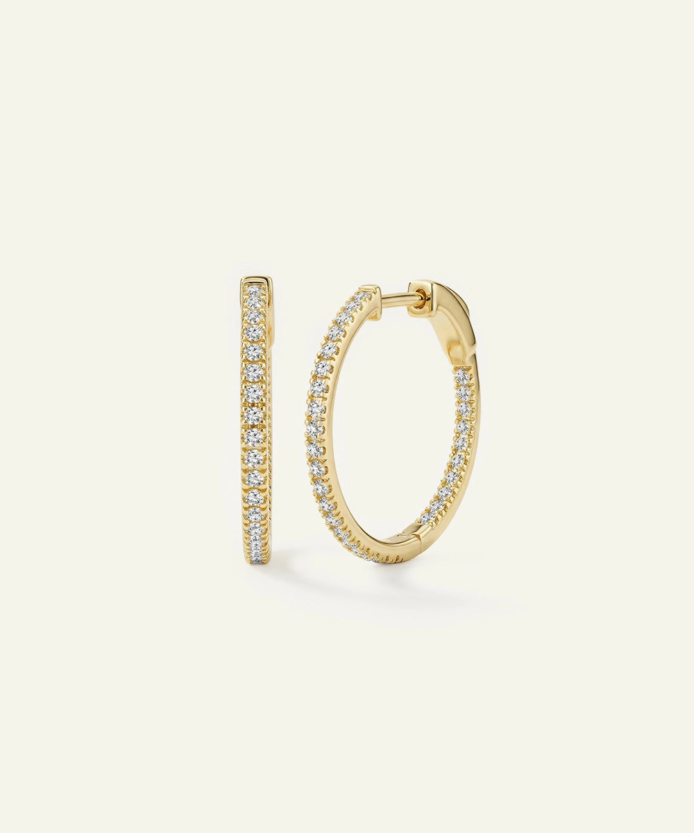 Gold hoop earrings with diamond accents on a light beige background