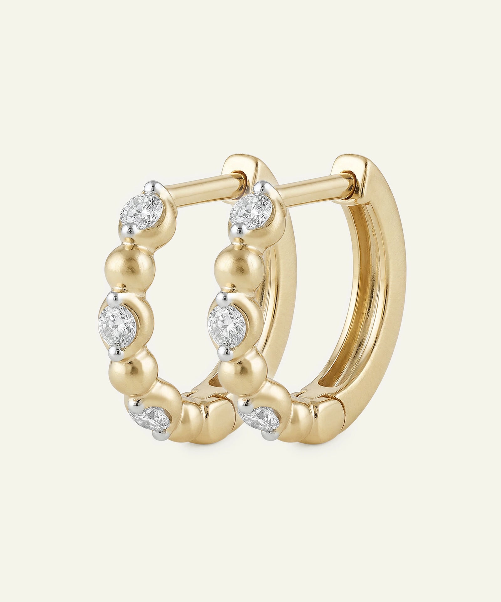 Gold hoop earrings with diamond accents on a light beige background