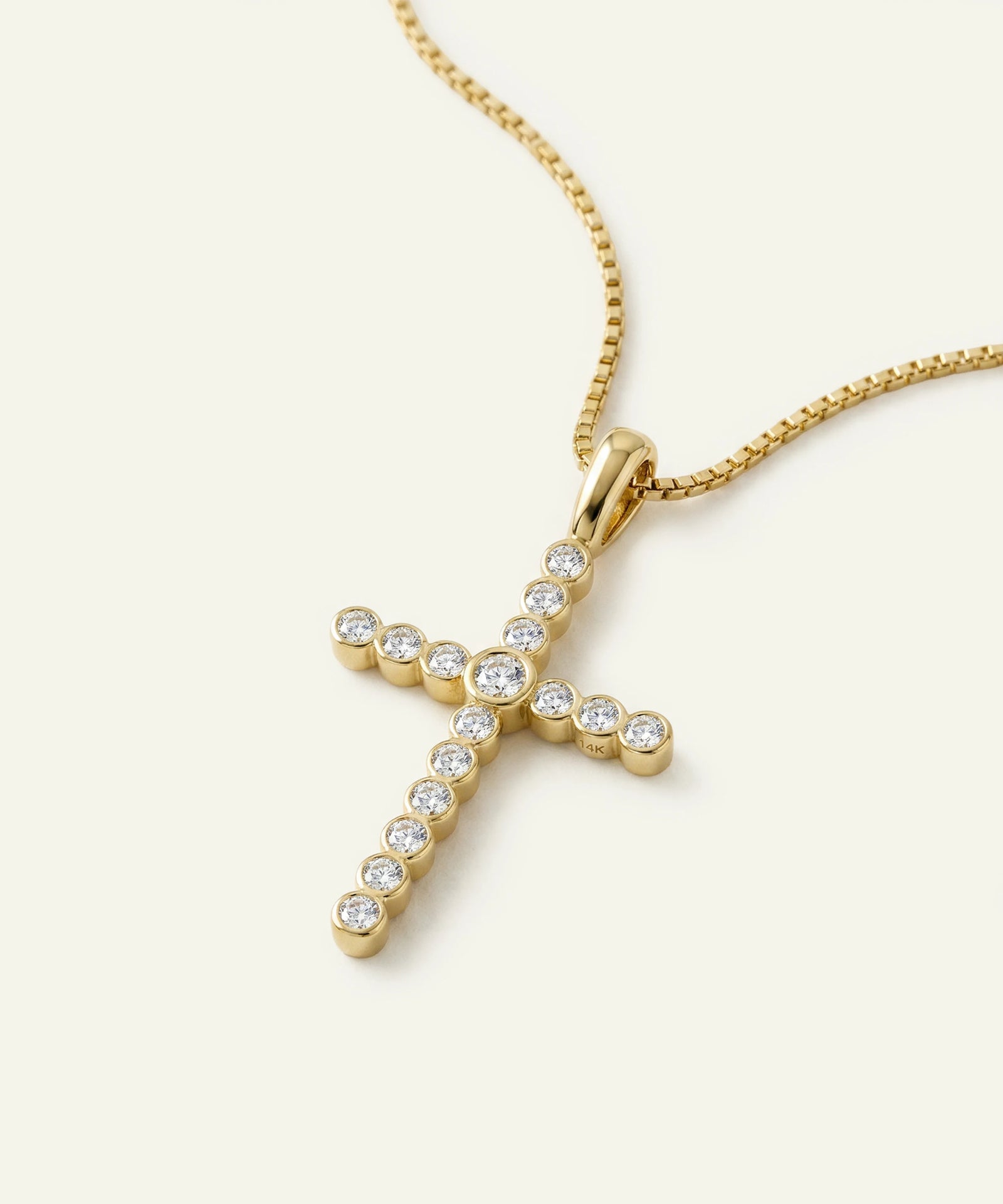 Gold cross pendant necklace with clear stones on a white background