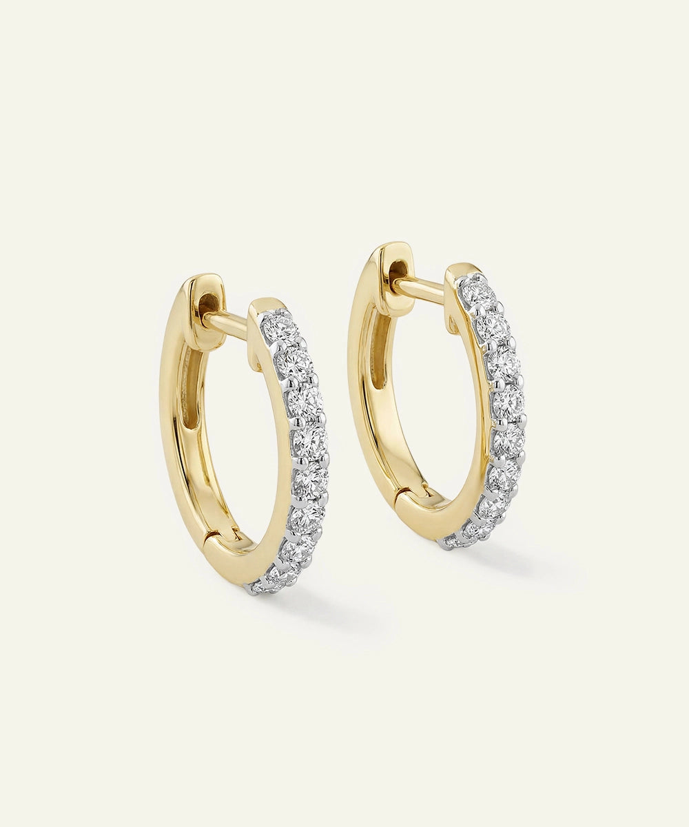 Gold hoop earrings with diamond accents on a light beige background