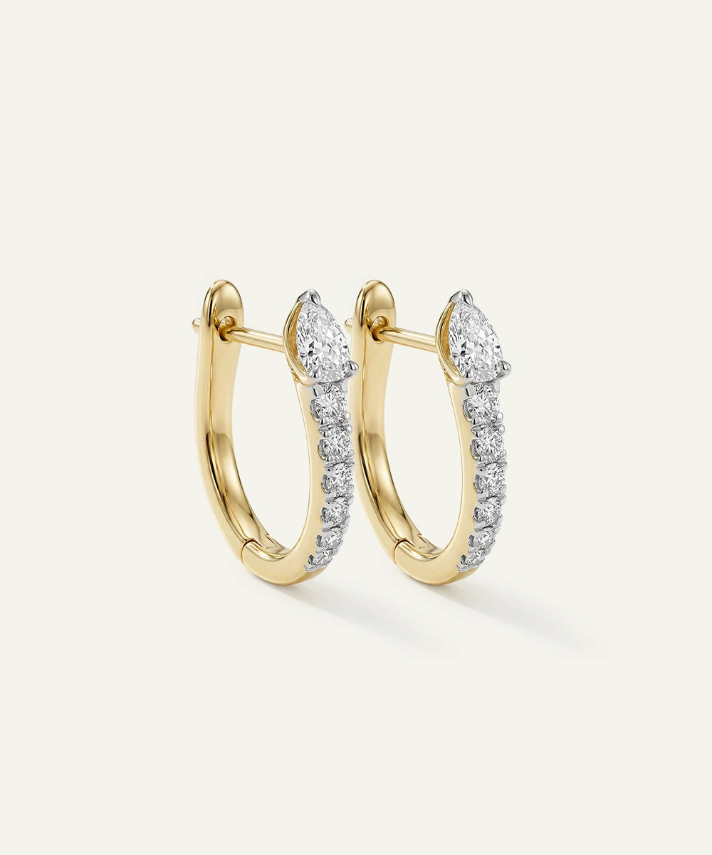 Gold hoop earrings with diamond accents on a light beige background