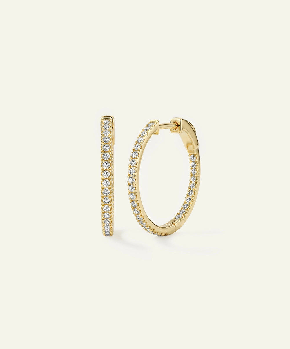 Gold hoop earrings with diamond accents on a light beige background