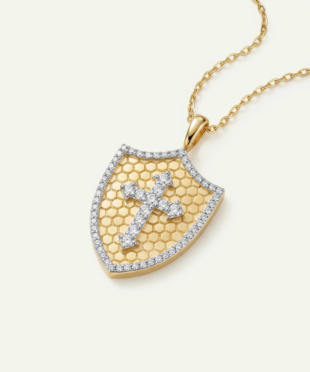 Gold necklace with a shield-shaped pendant featuring a cross design on a white background