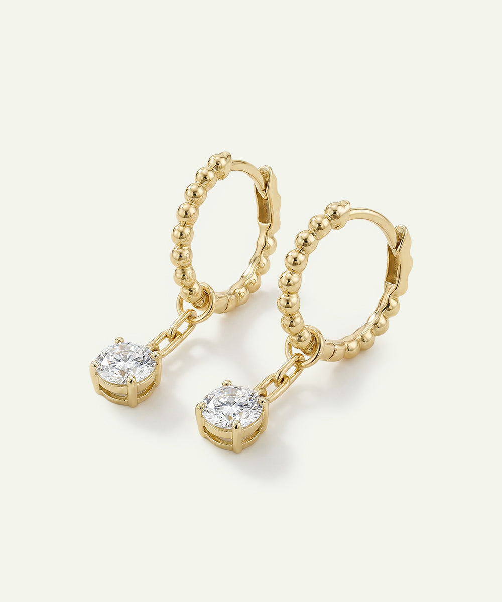 Gold hoop earrings with small round gemstones on a light background
