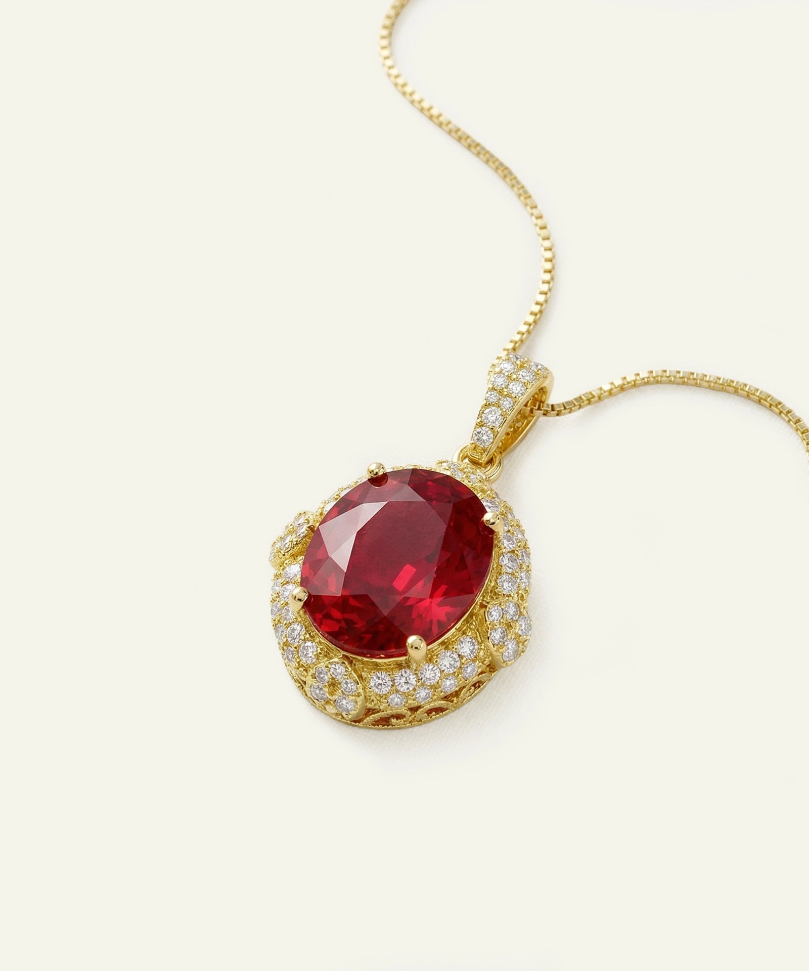 Oval ruby pendant necklace with a diamond halo in yellow gold.