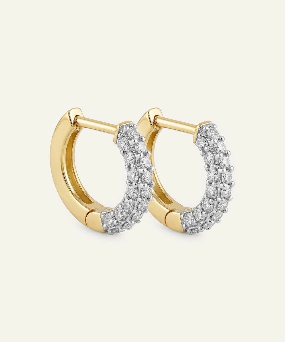 Gold hoop earrings with diamond accents on a light beige background