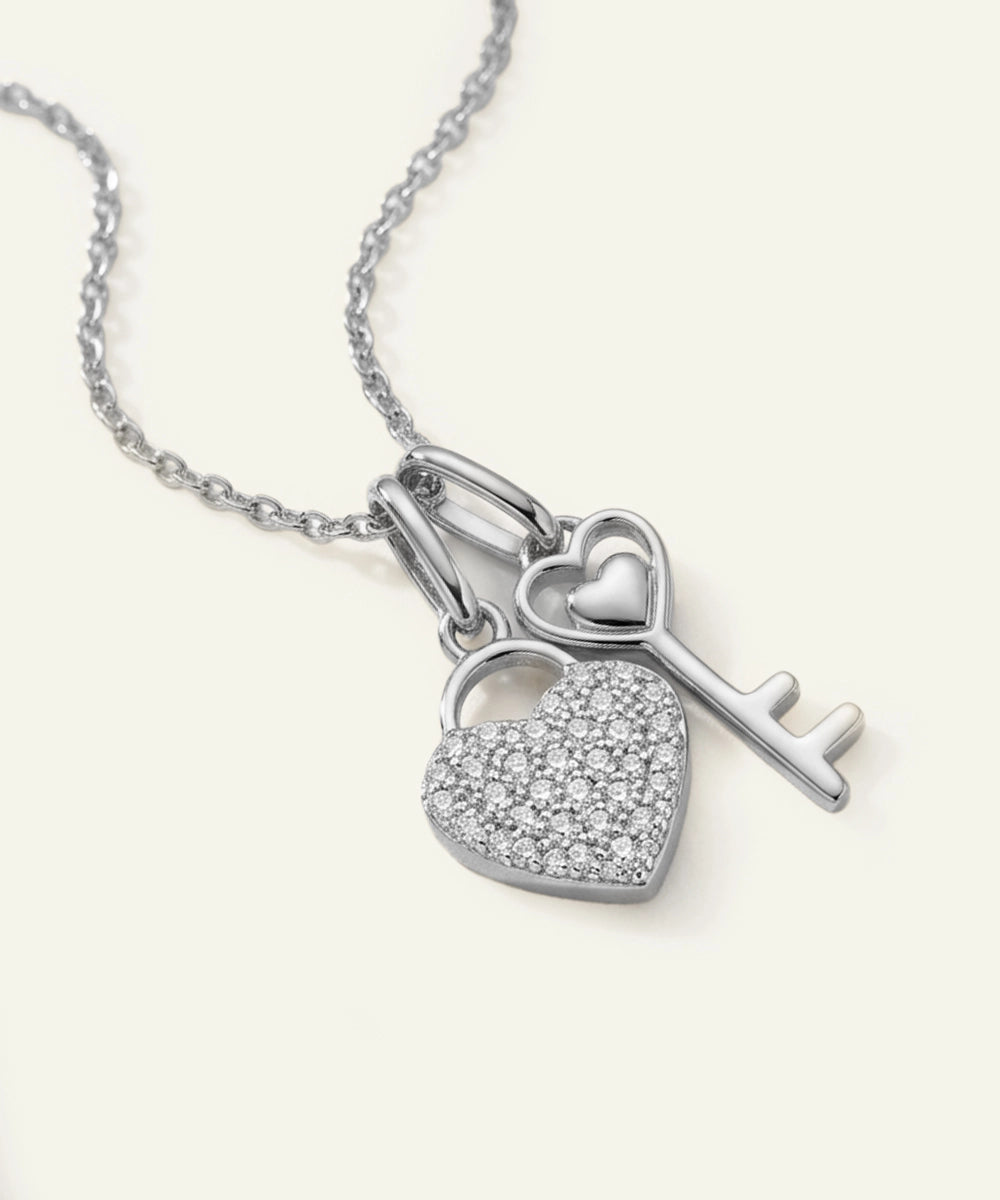Silver necklace with heart padlock and key charm on a white background