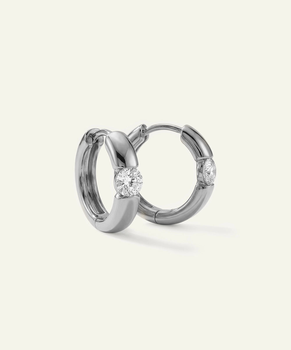 Pair of silver hoop earrings with embedded diamonds on a light gray background