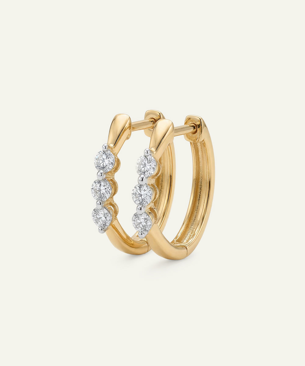 Gold hoop earrings with diamond accents on a light beige background