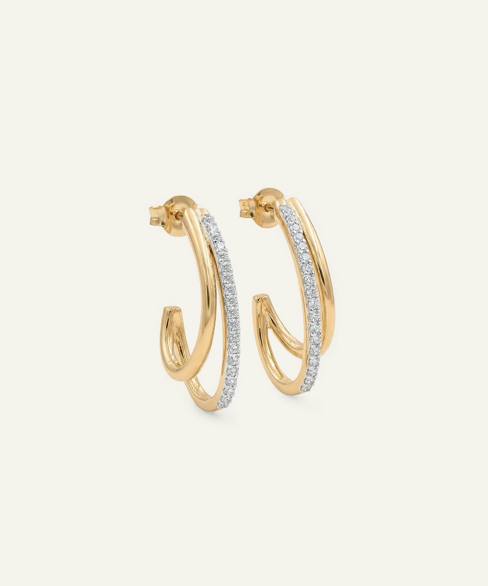 Gold hoop earrings with diamond accents on a light beige background