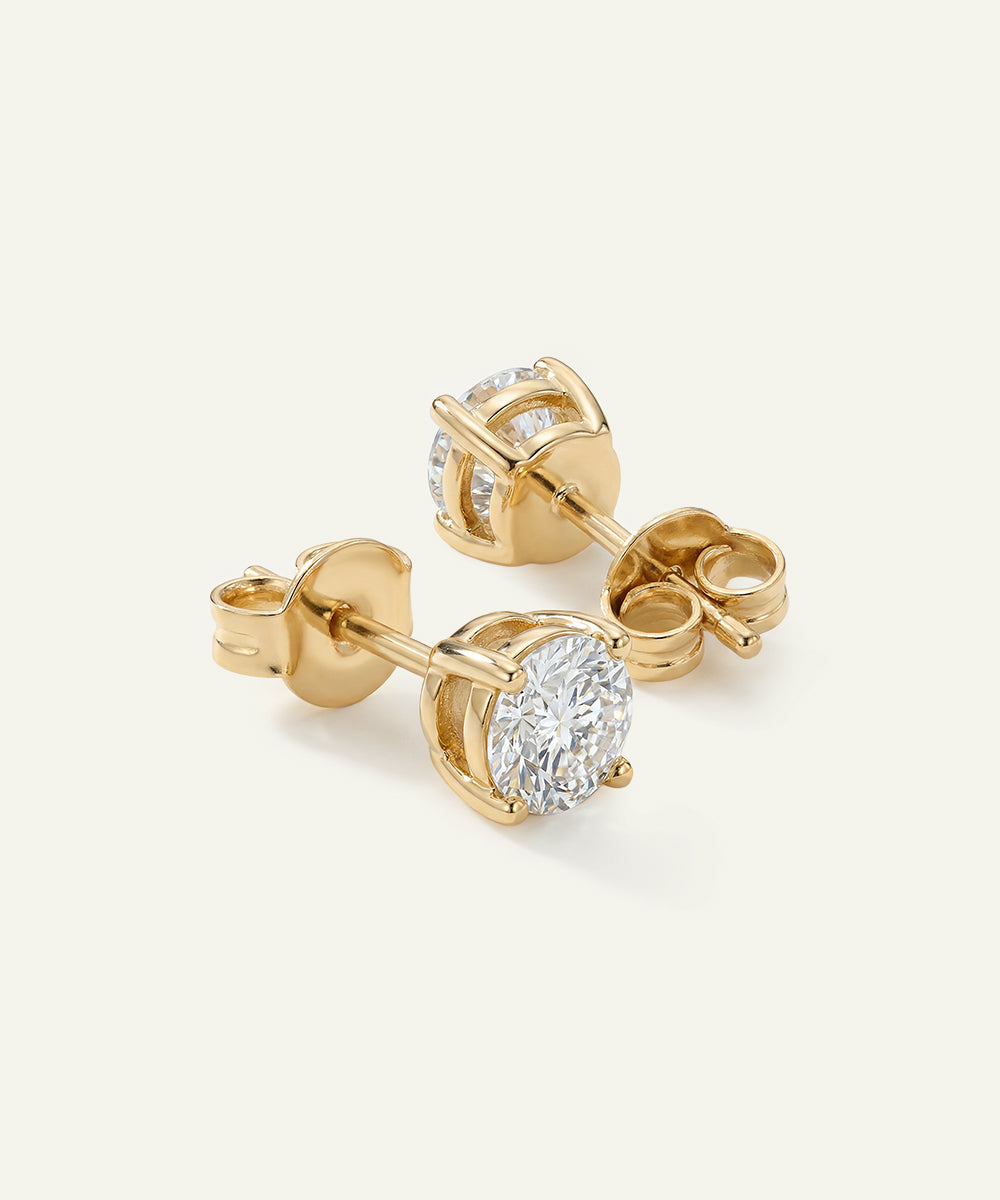 Gold diamond stud earrings on a light beige background
