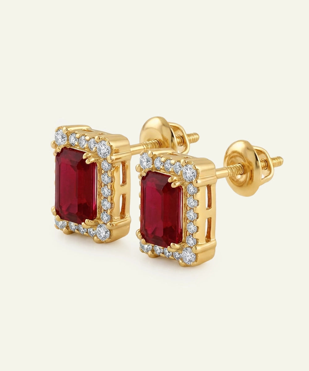 Gold earrings with red gemstones and diamond accents on a light beige background