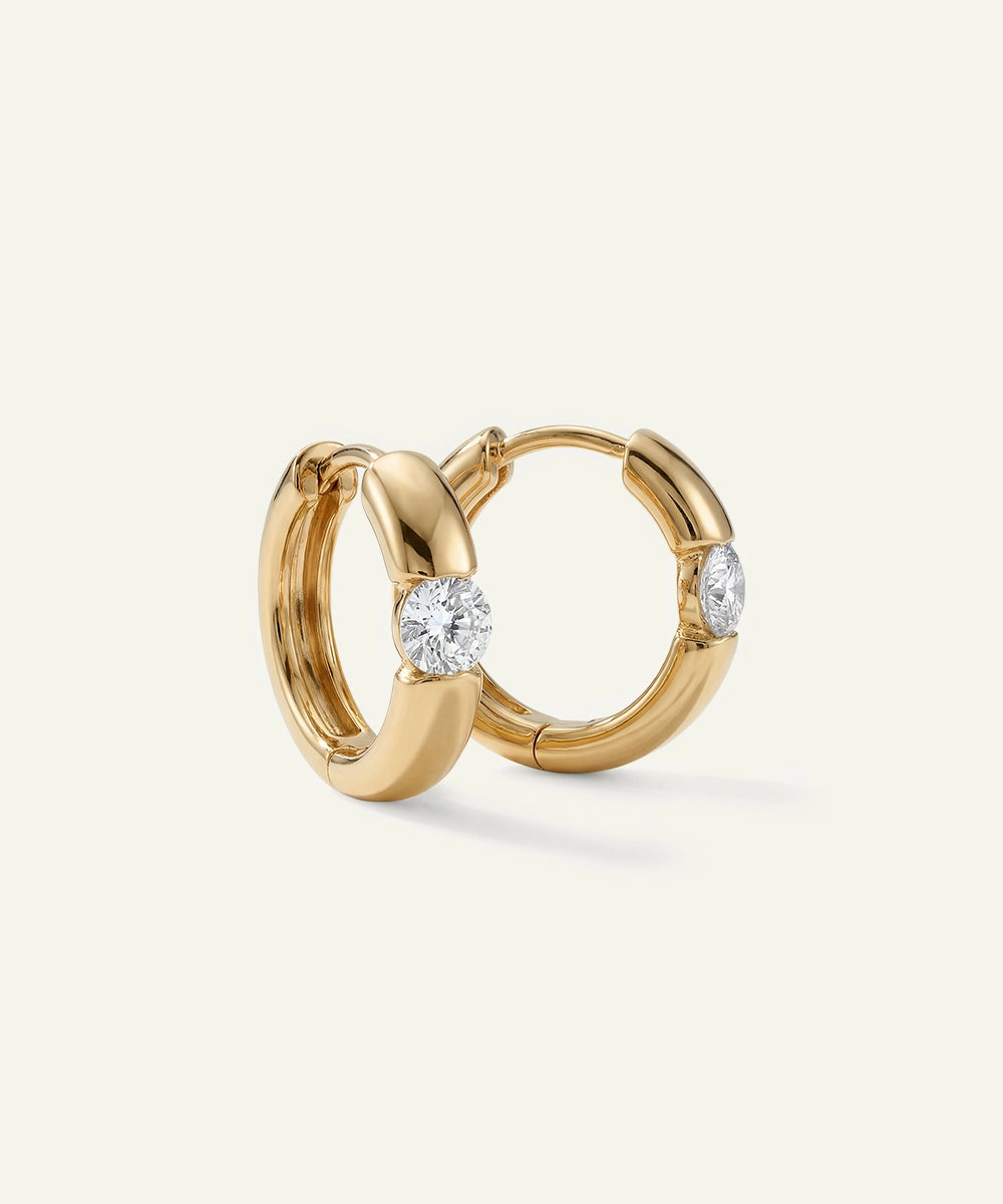 Gold hoop earrings with embedded diamonds on a light beige background