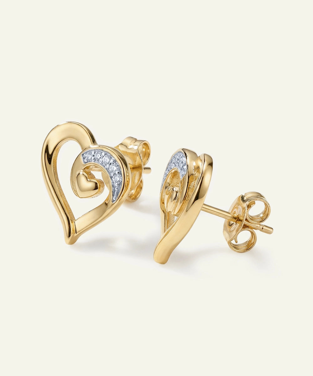 Gold heart-shaped earrings with diamond accents on a light beige background