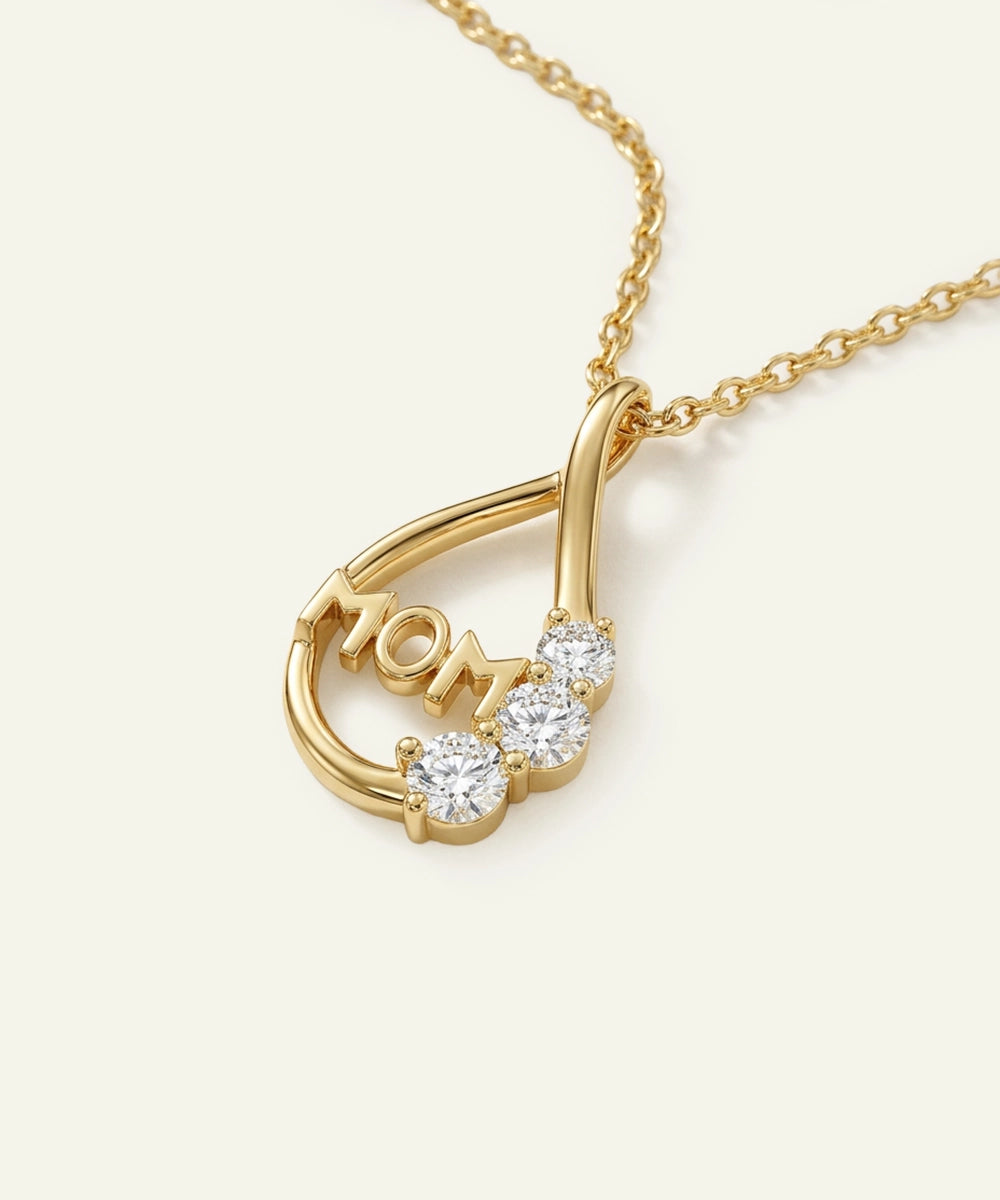 Gold necklace with 'MOM' pendant on a light beige background