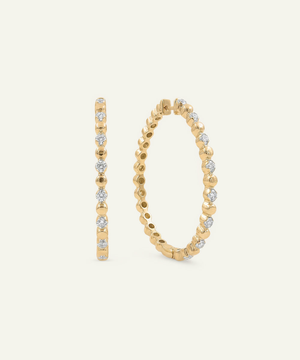 Gold hoop earrings with embedded diamonds on a light beige background
