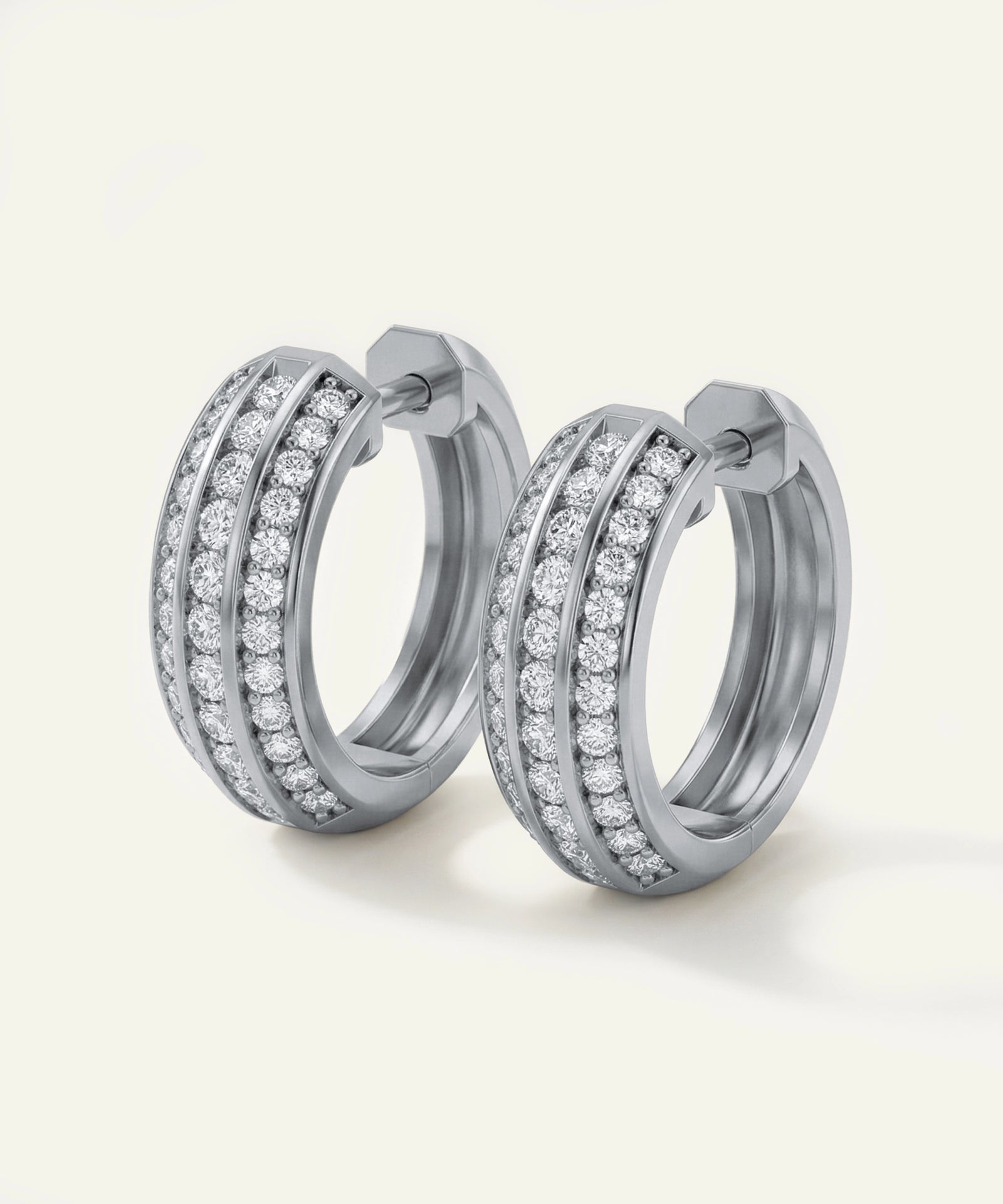 Pair of silver hoop earrings with clear gemstones on a light beige background