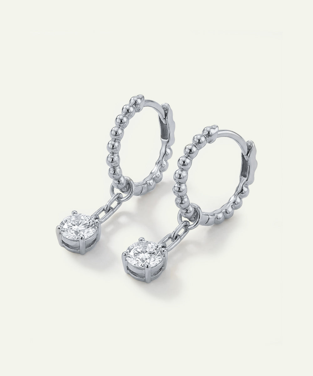 Pair of silver earrings with heart-shaped gemstones on a light gray background