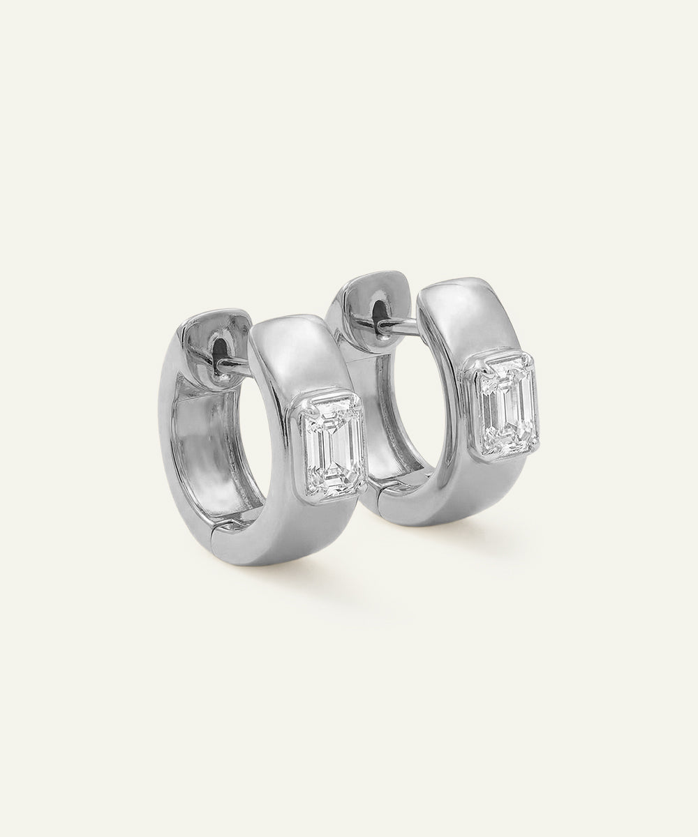 Pair of silver hoop earrings with emerald-cut gemstones on a white background