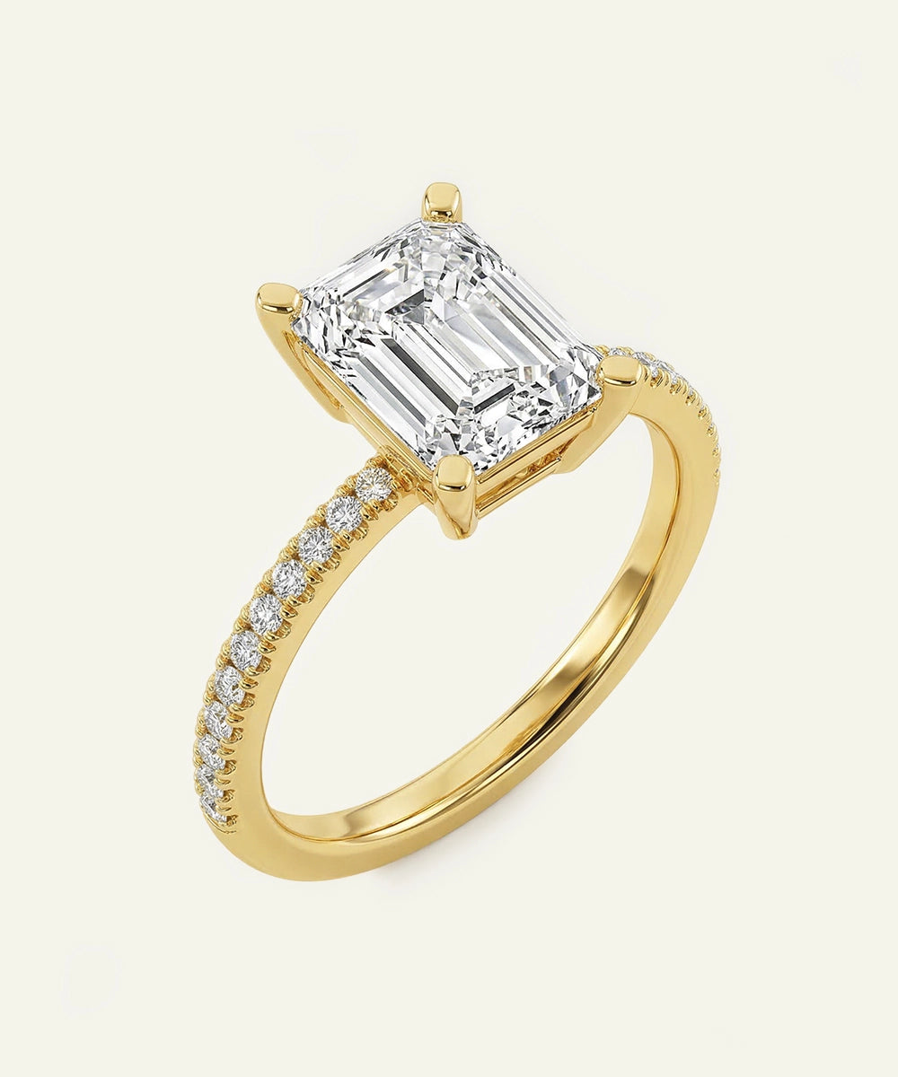 Gold ring with a large emerald-cut diamond and smaller diamonds on the band against a white background