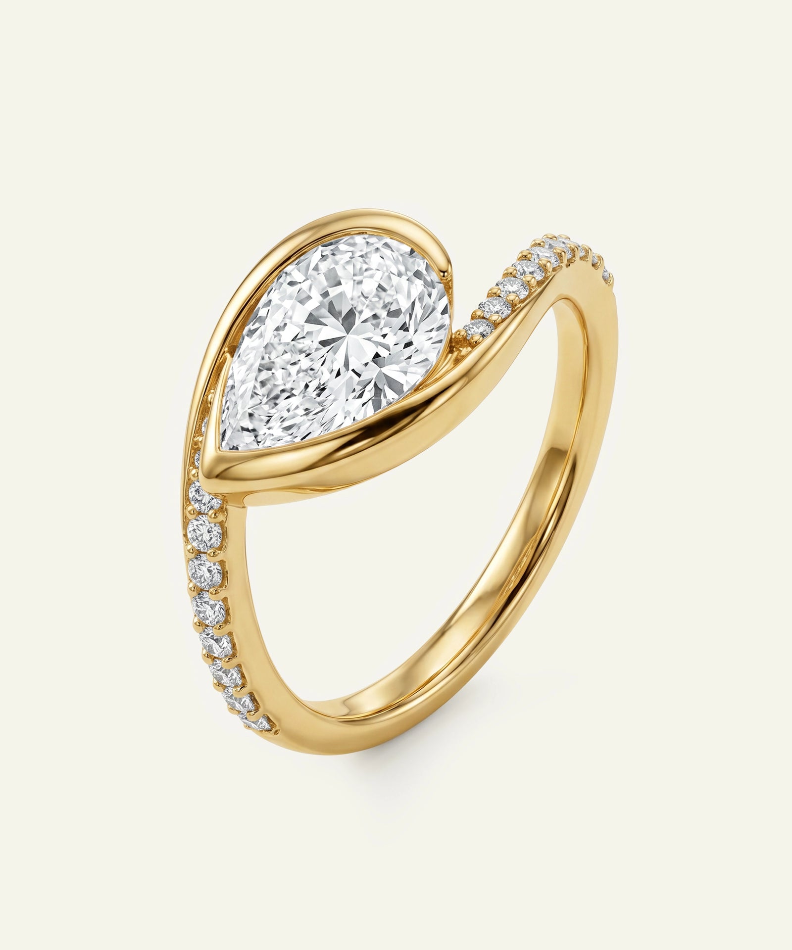 Gold ring with a pear-shaped diamond and smaller diamonds on a light beige background