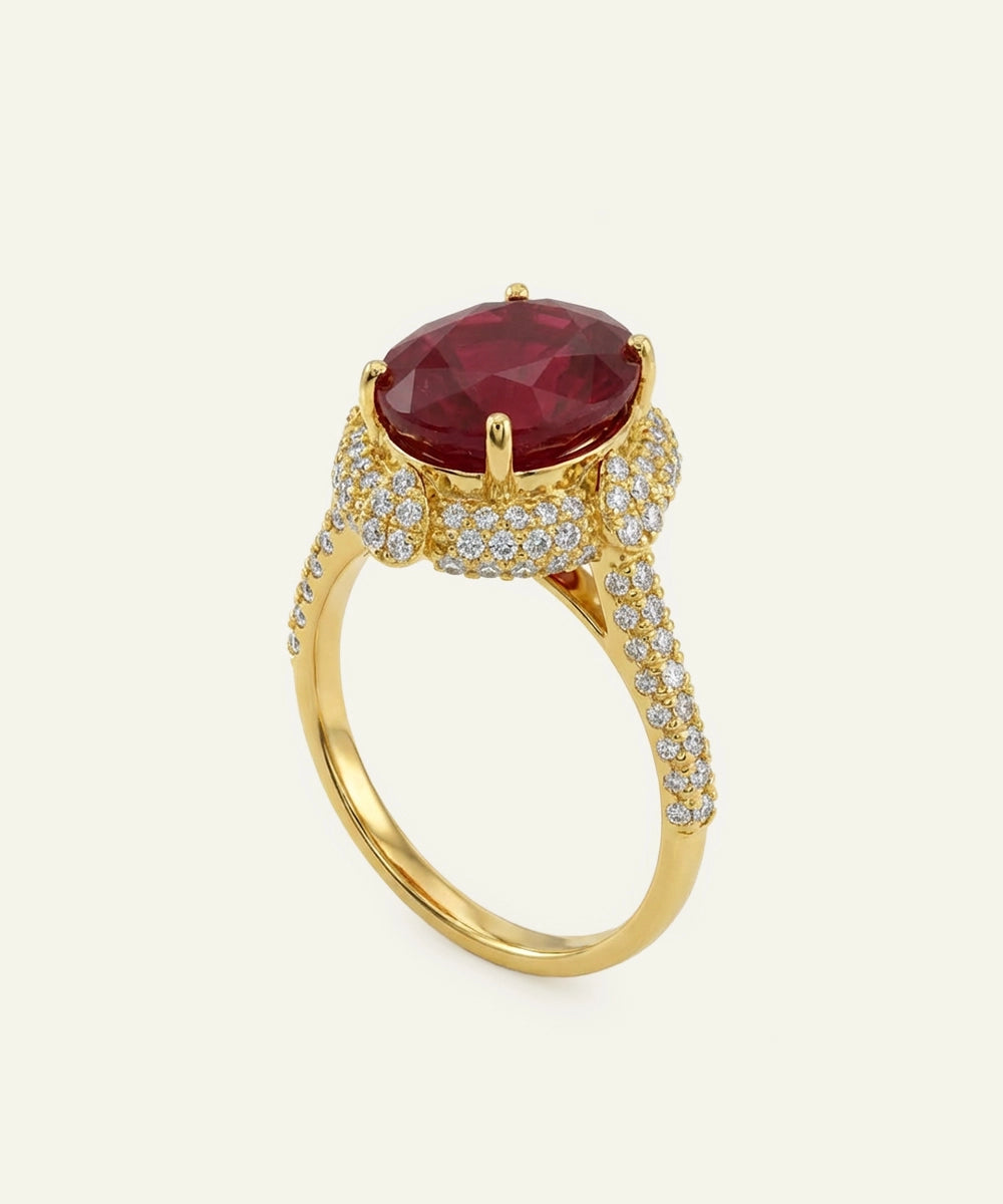 Gold ring with a large red gemstone and smaller diamonds on a light beige background