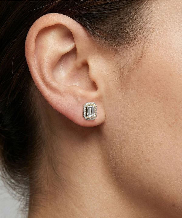 Close-up of an ear wearing a diamond earring with a neutral background