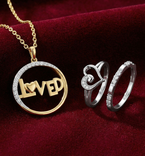 Gold “Loved” pendant necklace with diamond circle and white gold diamond heart rings displayed on red velvet